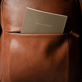 Brown leather backpack with a notebook inside on a dark background