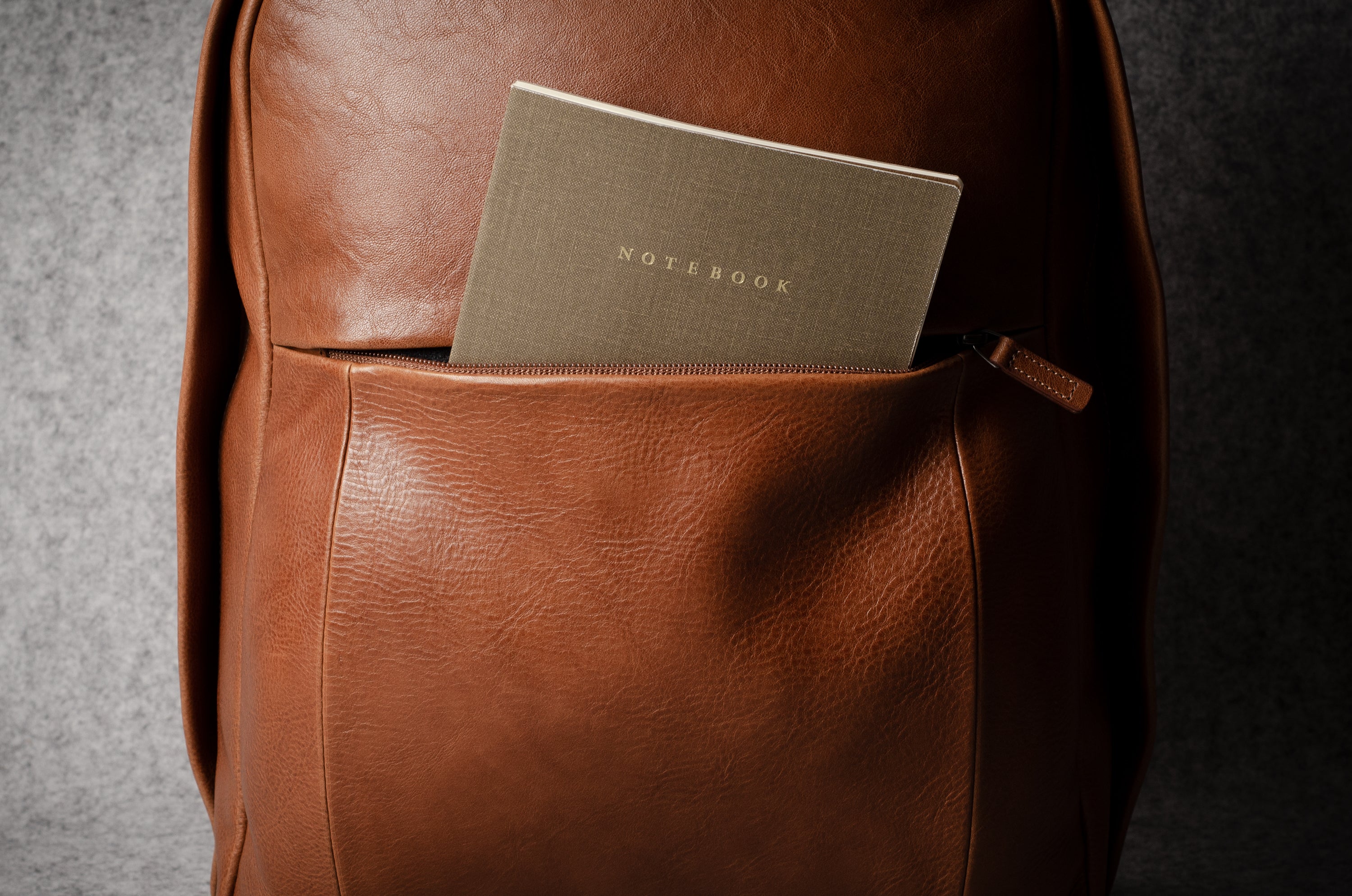 Brown leather backpack with a notebook inside on a dark background