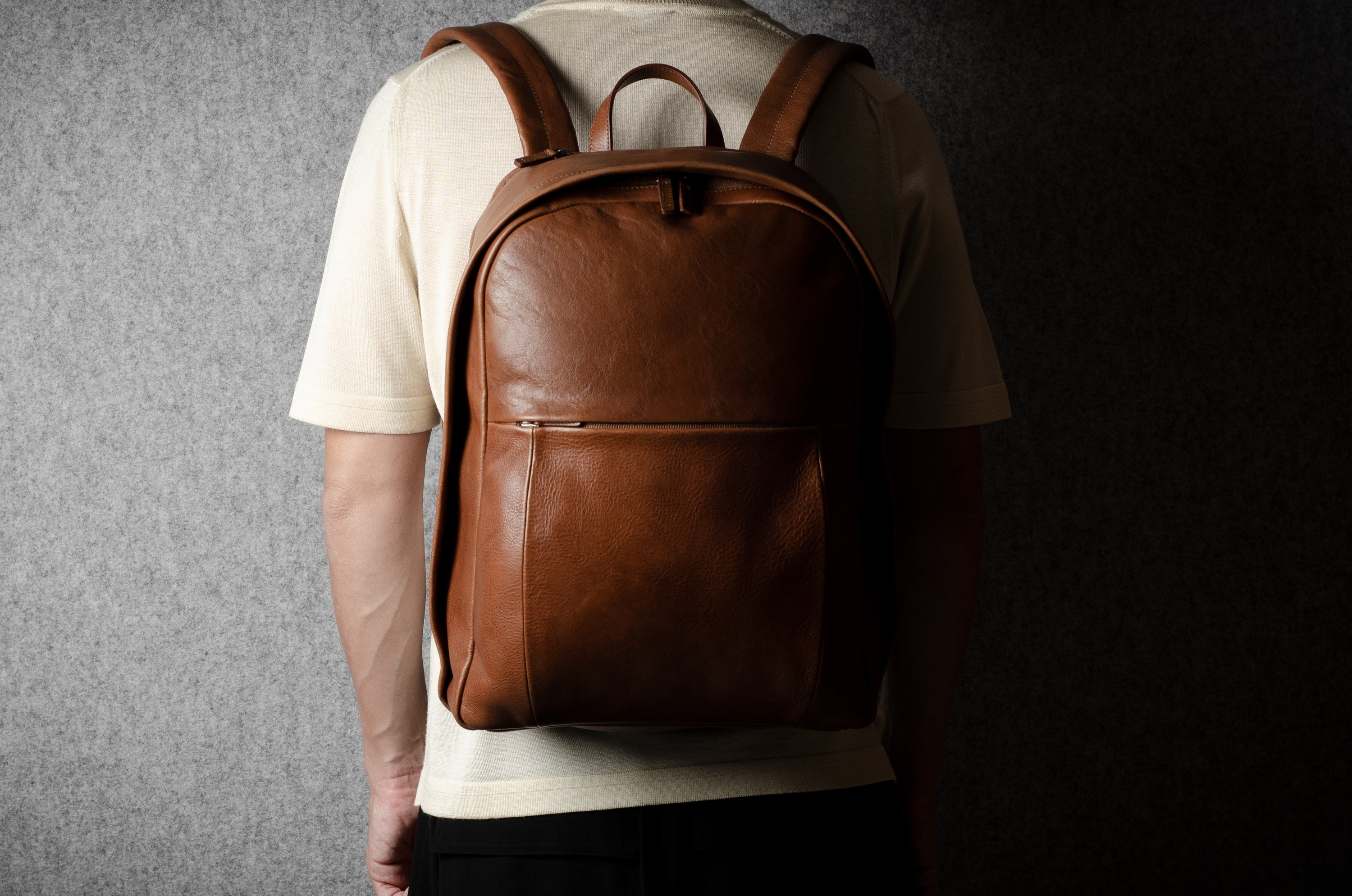 Person wearing a brown leather backpack against a dark background