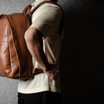 Person wearing a brown leather backpack against a dark background
