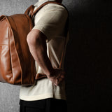 Person wearing a brown leather backpack against a dark background