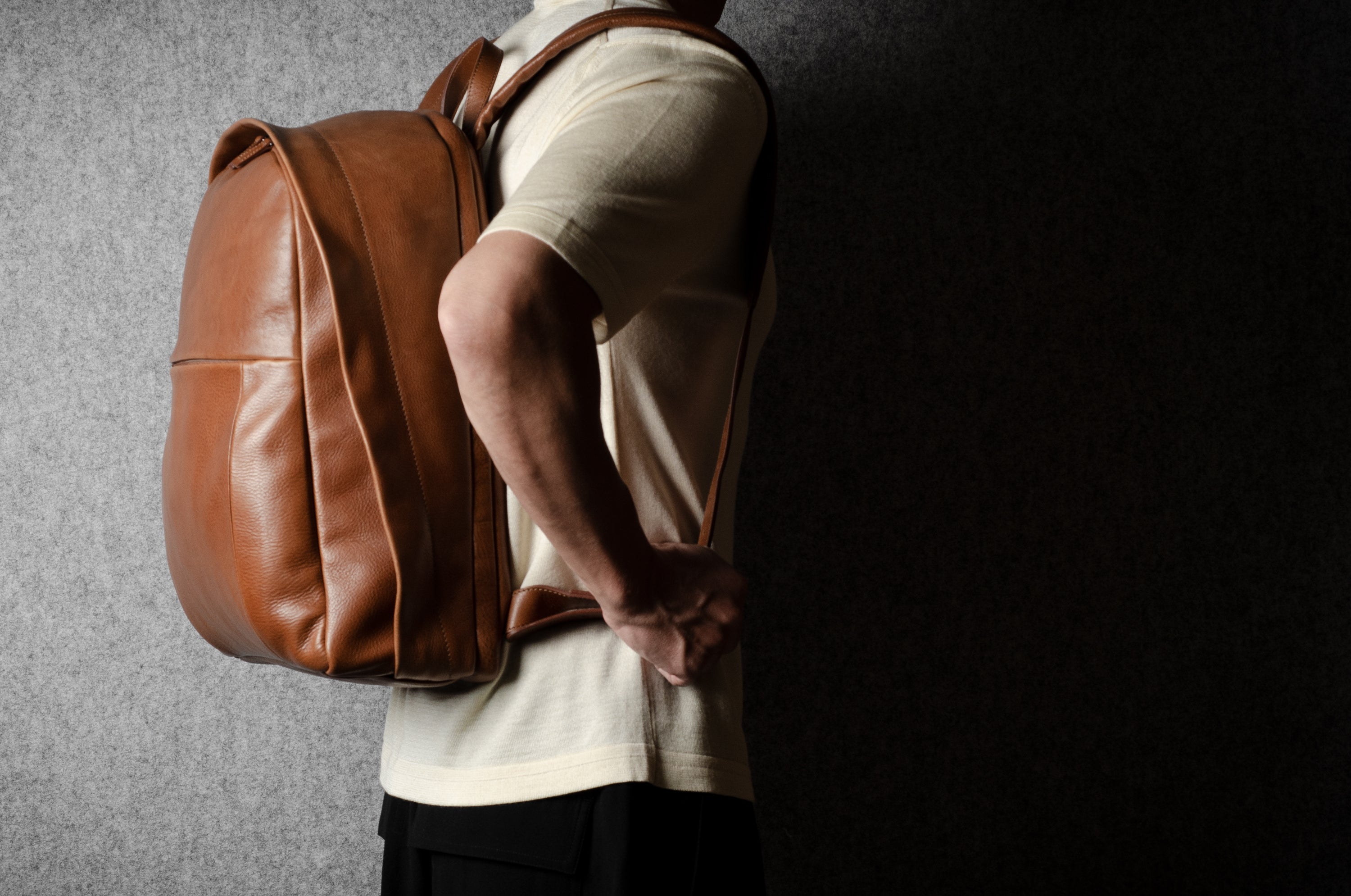 Person wearing a brown leather backpack against a dark background
