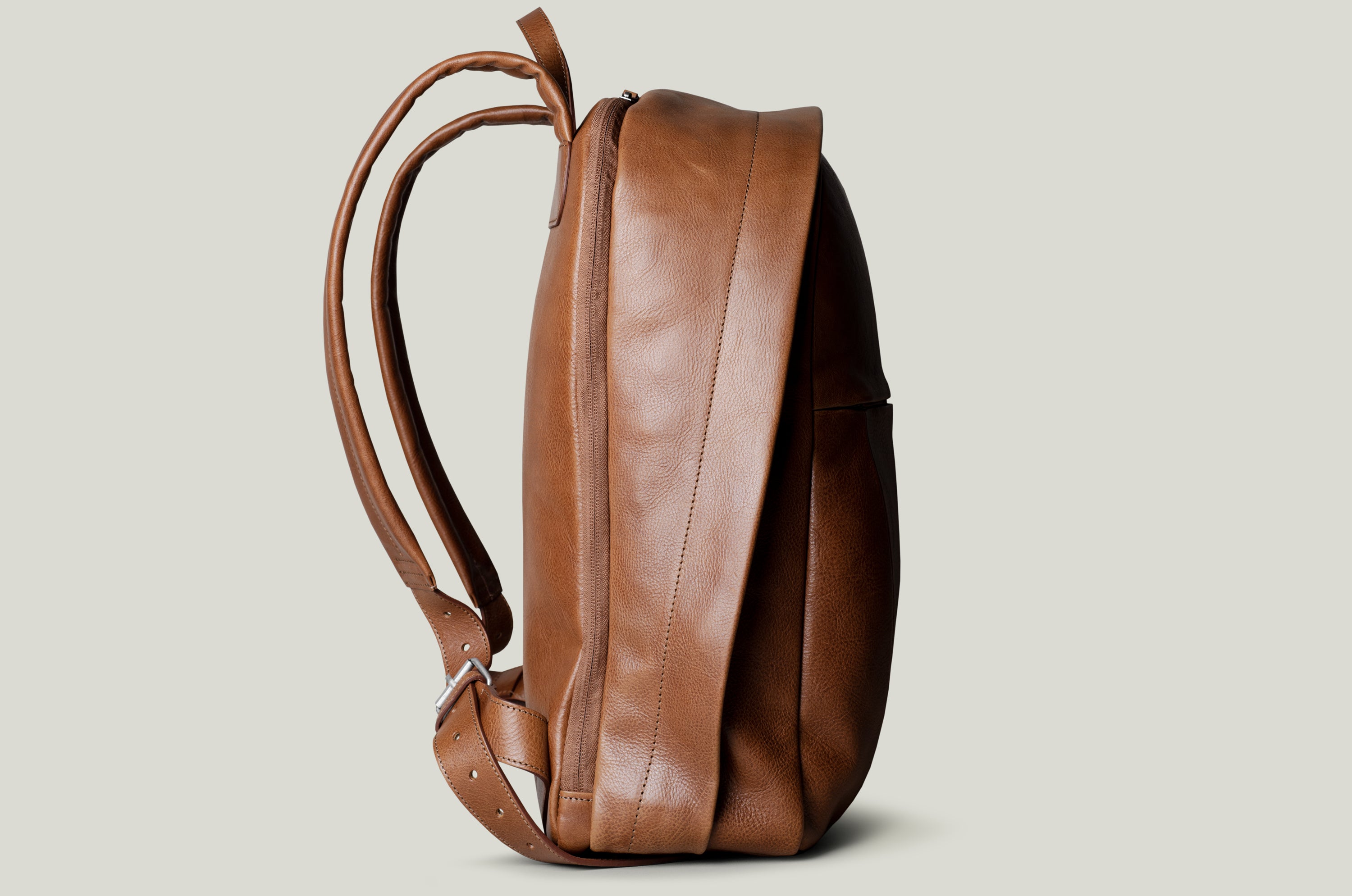A brown full leather backpack with two adjustable leather shoulder straps and a zippered closure.