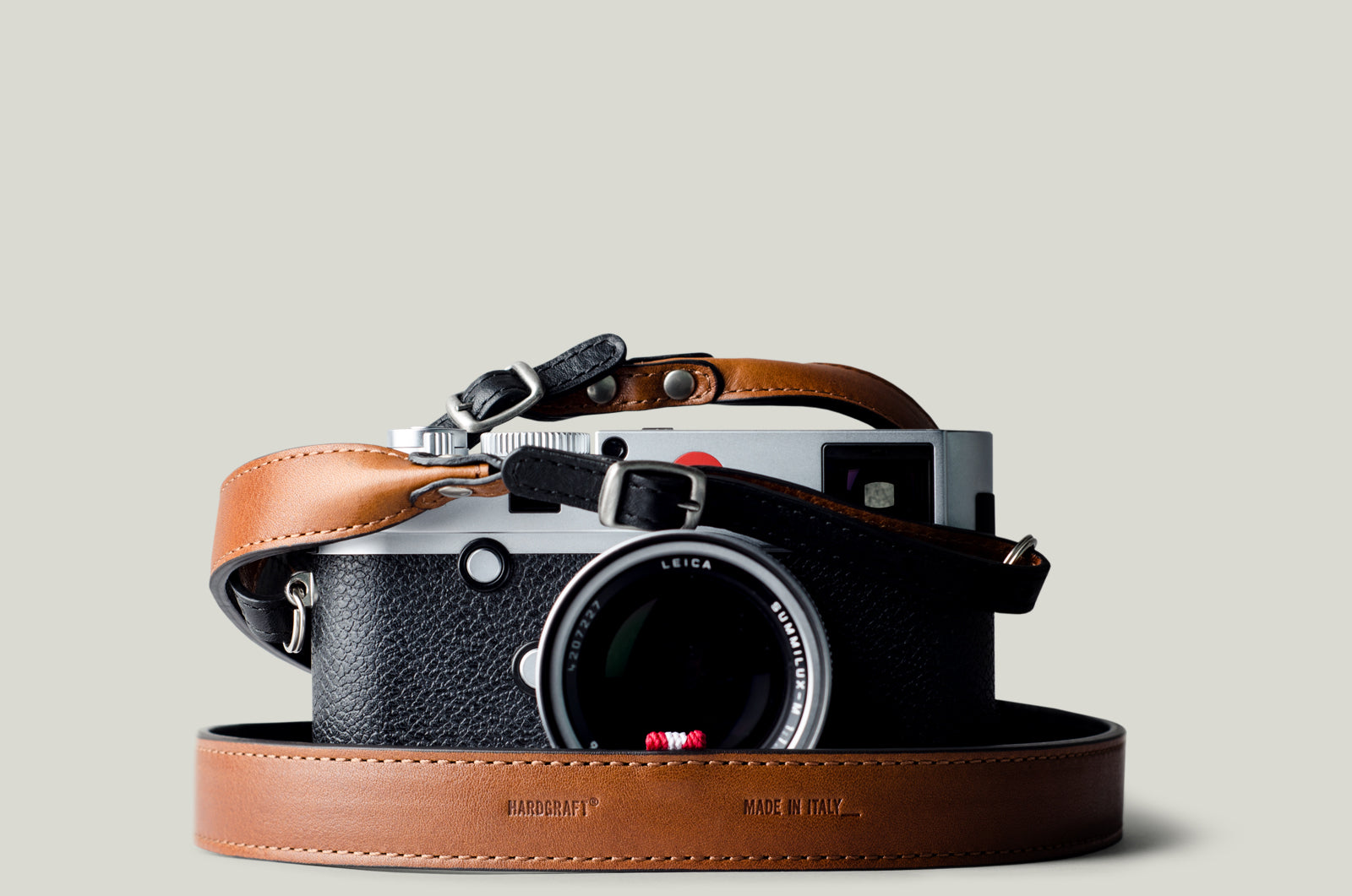 A camera with a brown and black duotone leather strap, designed to hang around the neck.