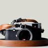 A camera with a brown and black duotone leather strap, designed to hang around the neck.